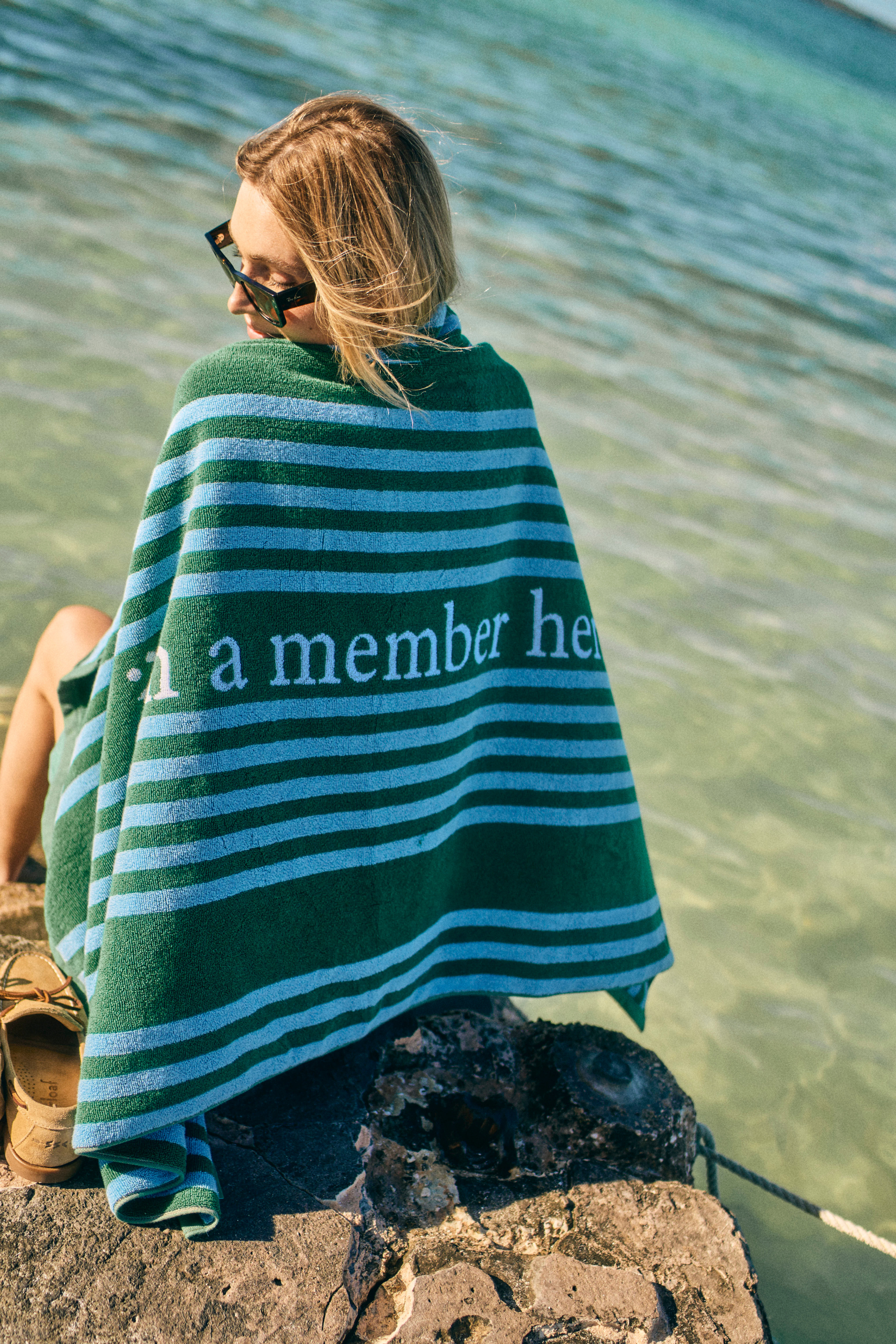 Person wrapped in a green and blue striped towel by a body of water